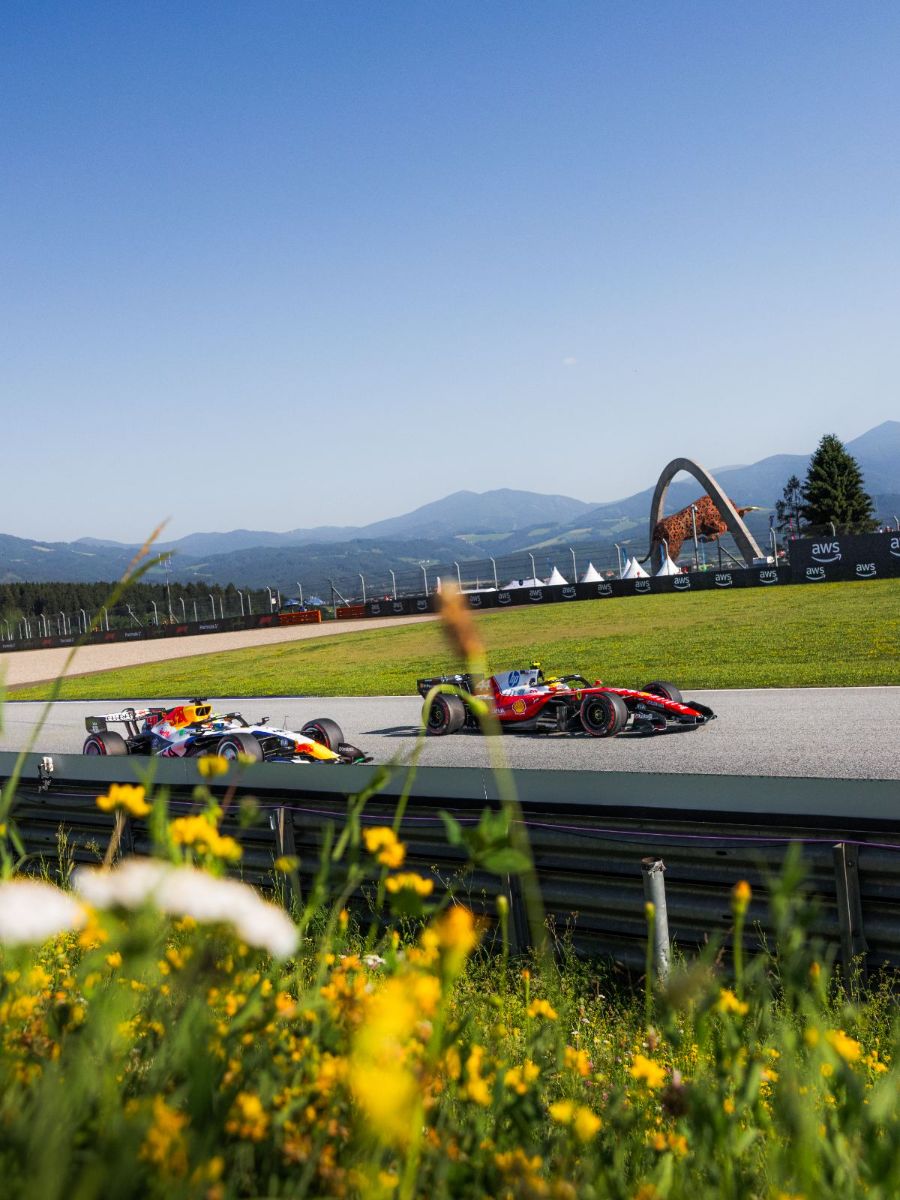 Grand Prix d'Autriche 2026, Red Bull Ring : Samedi · EL3 · Deux voitures sous le taureau du Red Bull Ring, fleurs au premier plan